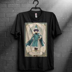 May include: Black t-shirt featuring a framed illustration of a character in a teal and white outfit, wearing a hat. The illustration has a vintage style with the word "AGOTT" at the bottom.