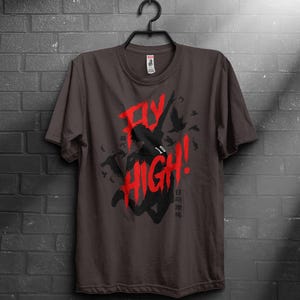 Puede incluir: Camiseta marrón oscuro con un gráfico rojo que dice "FLY HIGH!" y una silueta de una persona saltando. También es visible el número "10". También hay texto en japonés.