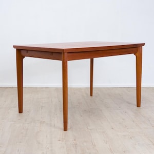 Könnte beinhalten: Ein rechteckiger Esstisch aus Holz mit einer warmen braunen Oberfläche. Der Tisch verfügt über eine glatte, flache Tischplatte und vier konisch zulaufende Beine, die von den Ecken nach außen verlaufen und eine stabile Basis bilden.
