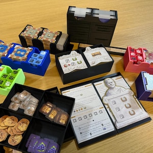 May include: A collection of board game components, including card holders in various colors like blue, green, pink, and purple. The image also shows cards, dice, and tokens, all neatly organized.