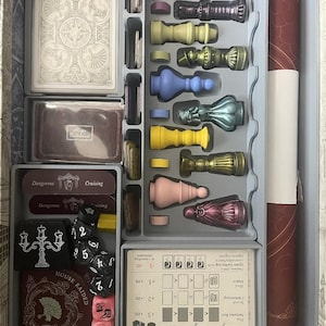 May include: A game board with a variety of game pieces, cards, and dice. The game pieces are in different colours, including purple, green, blue, yellow, pink, and red. The cards are in a variety of colours and have different designs. The dice are black and white.