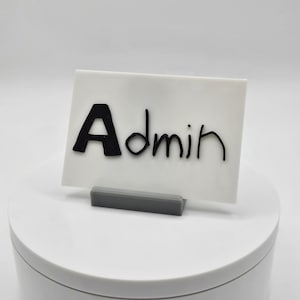 May include: White card with black text that reads "Admin" on a gray stand.