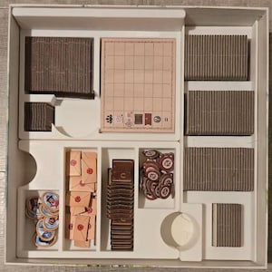 May include: A board game box insert containing organized game components. It features stacks of brown rectangular cards, a grid-patterned score pad, small tan envelopes with red wax seals, circular character tokens, and brown square tiles.
