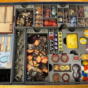 May include: A gray plastic organizer with compartments for storing game pieces. The organizer has labels for "CH", "II", "IV", and "Ally". The compartments contain various game pieces, including dice, tokens, and cards.