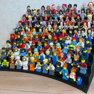 May include: A black tiered display stand holding a large collection of small plastic minifigures. The figures feature diverse hair colors, clothing styles, and accessories, arranged in rows on the stepped shelves of the black plastic organizer.