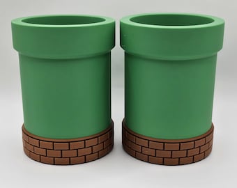 May include: Two green and brown ceramic cups shaped like a pipe. The cups have a brick pattern around the bottom.