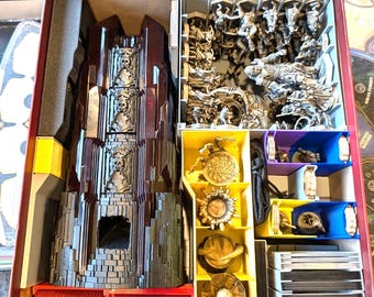May include: A board game organizer with compartments filled with game pieces. The organizer is red with yellow, blue, and purple inserts. The game pieces include miniature figures, tokens, and a castle-like structure.