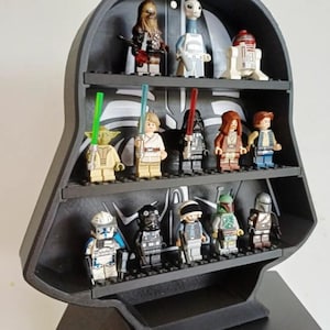 May include: A black, helmet-shaped display stand with three horizontal shelves, designed to hold small plastic figures. The back panel features a stylized graphic of a mask. The shelves are populated with thirteen various miniature character figures.