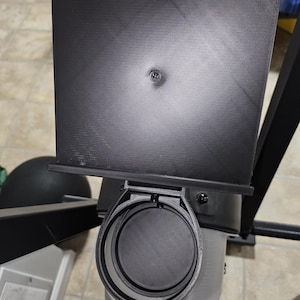 May include: A black 3D printed cup holder with a black plastic lid. The cup holder is attached to a black metal frame.