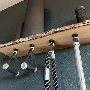 May include: A wooden shelf with five hooks, holding a black yoga mat, a black rope, two black exercise bands, and a silver pole. The shelf is mounted on a dark blue wall.