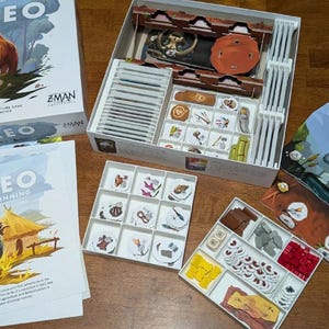 May include: Paleo board game box and components. The box features a mammoth illustration. Game pieces and cards are visible, including a game board and various tokens. The game is by Z-Man Games.