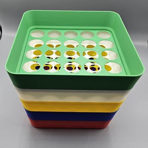 May include: A multi-layered storage container with a green top featuring circular openings. The layers are in various colors: green, white, yellow, blue, and red. The interior shows a pattern of yellow circles with red and blue dots.