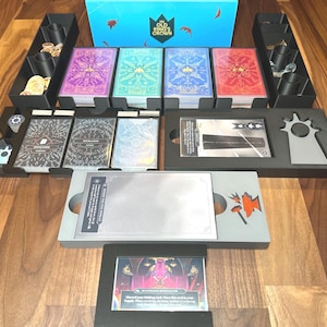 May include: A board game set with various components, including cards, tokens, and storage trays. The game box is blue with the text "OLD KING'S CROWN". The cards feature colorful designs, and the set includes black and gray trays for organization.
