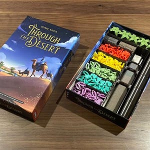 May include: Board game box titled "Through the Desert" with a desert scene illustration. The open game box reveals colorful game pieces in red, yellow, green, blue, and purple. Includes silver and black game components.