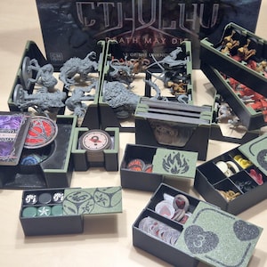 May include: An organized board game storage solution with various compartments and trays. The set includes figures, cards, and tokens, all neatly arranged in black and green containers. The game box, titled "Cthulhu Death May Die," is visible in the background.