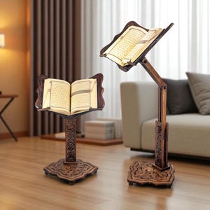 May include: Two dark brown wooden book stands with intricate carved patterns on the base and central pillar. Each stand features an adjustable ledge holding an open book with visible text. The stands have a sturdy square base and a vertical support.