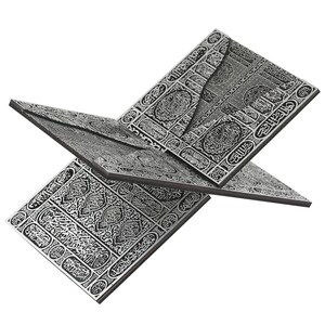 May include: A silver-colored book stand with intricate, engraved patterns and Arabic calligraphy. The stand is designed to hold a book open, with multiple panels angled for display. The design is detailed and ornate.