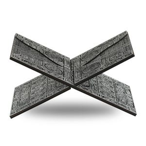 May include: A dark gray wooden book stand with intricate, engraved patterns. The stand is designed to hold a book open, with two panels forming an X shape. The detailed carvings are in a lighter gray, creating a contrast against the darker background.