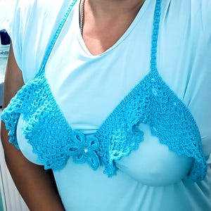 Puede incluir: Un top de ganchillo azul claro con un adorno floral. El top presenta un diseño de cuello halter y un borde festoneado. El trabajo de ganchillo es intrincado, con un delicado patrón de tejido abierto.
