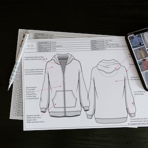 Puede incluir: Un dibujo t&eacute;cnico de una sudadera con capucha y cremallera. El dibujo incluye detalles como el tipo de cremallera, las costuras y el bolsillo. El texto del dibujo dice "Stacked herringbone tape as BNT DTM Dream Blue lpg 21".