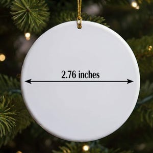 A white ornament with a measurement line on it, hanging on a Christmas tree.