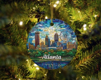 May include: Round Christmas ornament featuring a colorful stained-glass design of the Atlanta skyline, including the Ferris wheel and skyscrapers. The word "Atlanta" is written in white script across the bottom. The ornament hangs from a gold string.