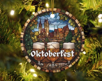 May include: Round Christmas ornament with a stained-glass design featuring three beer glasses in front of a German village scene. The word "Oktoberfest" is written across the bottom in white letters. The ornament hangs from a gold string.