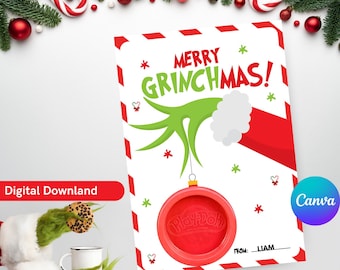 May include: A printable Christmas card featuring the Grinch's hand holding a red ornament with the word "Play-Doh" on it. The card has a red and white striped border and the text "Merry Grinchmas!" in green and red letters.