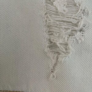 Puede incluir: Primer plano de una tela vaquera azul claro con un gran agujero desgastado. La tela tiene un patr&oacute;n de tejido diagonal.