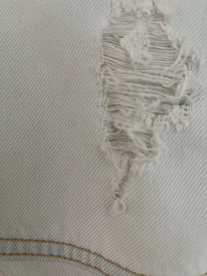 Puede incluir: Primer plano de una tela vaquera azul claro con un gran agujero desgastado. La tela tiene un patr&oacute;n de tejido diagonal.