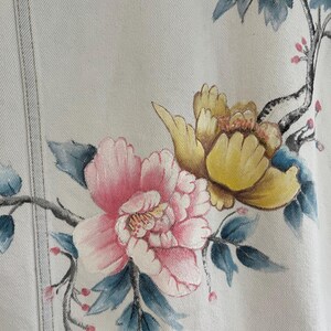 Puede incluir: Una chaqueta vaquera blanca con dise&ntilde;os florales pintados a mano. Las flores son rosas, amarillas y azules. La chaqueta tiene una textura sutil.