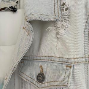 Puede incluir: Una chaqueta vaquera azul claro con detalles desgastados y un solo bot&oacute;n en el bolsillo delantero. La etiqueta dice "Colin's Jeans" y "Talla M".