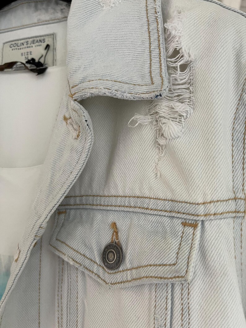 Puede incluir: Una chaqueta vaquera azul claro con detalles desgastados y un solo bot&oacute;n en el bolsillo delantero. La etiqueta dice "Colin's Jeans" y "Talla M".