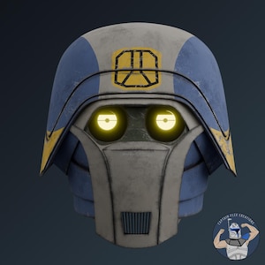 Puede incluir: Un casco desgastado con un esquema de colores azul y blanco roto, con un emblema amarillo en la frente. El casco tiene dos lentes oculares circulares de color amarillo brillante y una placa frontal vertical con una rejilla negra.