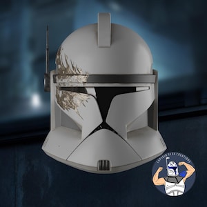 May include: A white and gray Clone Trooper helmet with a black visor and antenna. The helmet has gold-colored weathering details and a rectangular top piece. The image includes a logo in the bottom right corner.