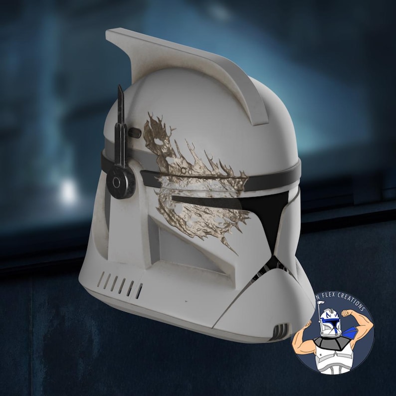 May include: A white and gray helmet with black accents and a gold-colored design. The helmet has a distinctive shape with a visor and a fin on top. The design is reminiscent of a clone trooper helmet.