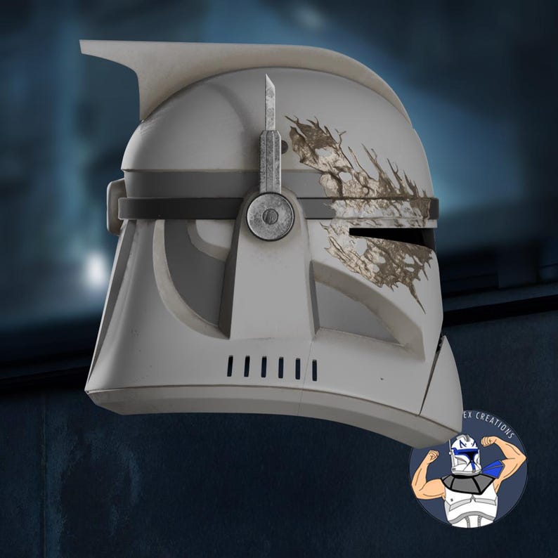 May include: A white and gray helmet with battle-worn details, featuring a distinctive visor and ventilation slits. The helmet has a dark gray band and a silver-colored attachment. A logo with a cartoon character is in the bottom right corner.