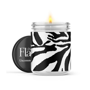 May include: A black and white zebra print candle in a glass jar with a black lid. The lid has the text "Uncommon Flames" on it.