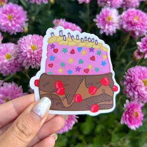 May include: A pink and brown cake with sprinkles, cherries, and worms. The cake is decorated with pink hearts and stars. The cake is on a white background.