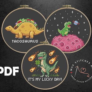 Puede incluir: Tres patrones de punto de cruz con diseños de dinosaurios adorables. El primer patrón muestra un dinosaurio verde con un taco en la espalda, el segundo muestra un dinosaurio verde sosteniendo un trébol de cuatro hojas, y el tercero muestra un dinosaurio verde en un planeta rosa con estrellas en el fondo. Los patrones se titulan "Tacosaurus", "¡Es mi día de suerte!" y "Max Stitches Art Patrones de punto de cruz".