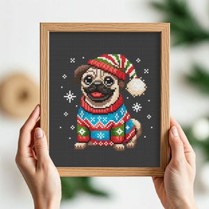 May include: Cross stitch pattern of a pug wearing a red and green Santa hat and a blue and red sweater with a snowflake pattern. The pug is on a dark gray background with white snowflakes.
