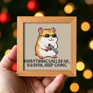 Puede incluir: Arte de punto de cruz en un marco de madera. La obra presenta un hámster con gafas de sol y una pistola. El texto dice: "EVERYTHING WILL BE OK, U A DIVA, KEEP GOING."