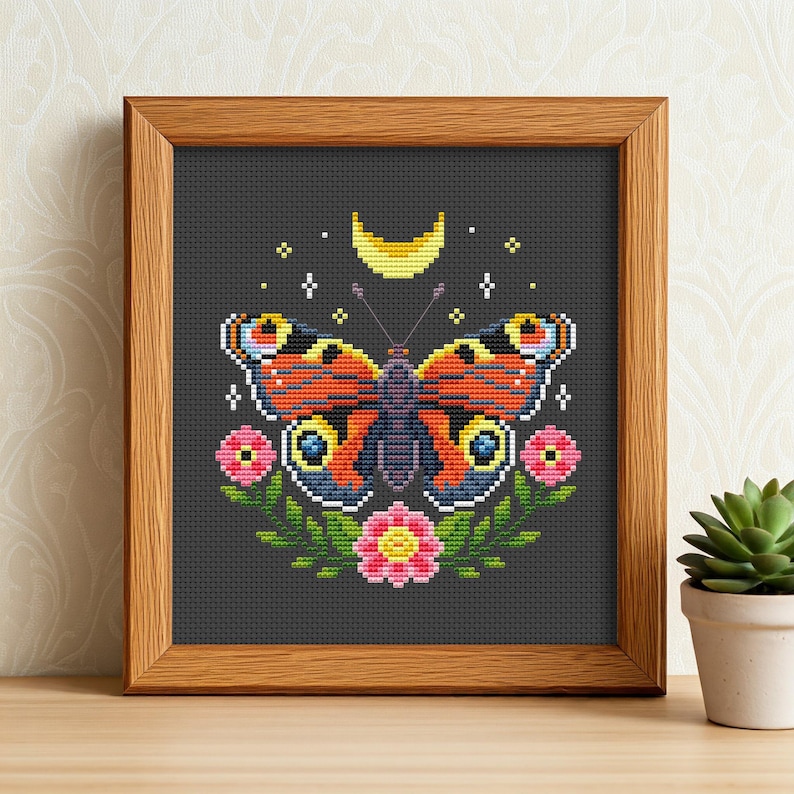 May include: A cross-stitch pattern featuring a colorful butterfly with a crescent moon and floral accents on a dark gray background.
