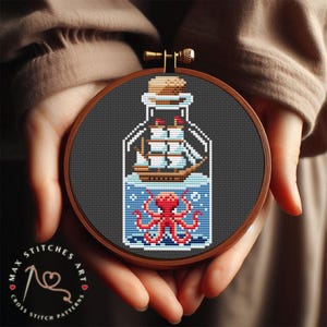 May include: A round wooden embroidery hoop with a black background. Inside the hoop is a cross stitch design of a glass bottle with a ship and an octopus inside. The bottle is blue and white, the ship is brown, and the octopus is red.