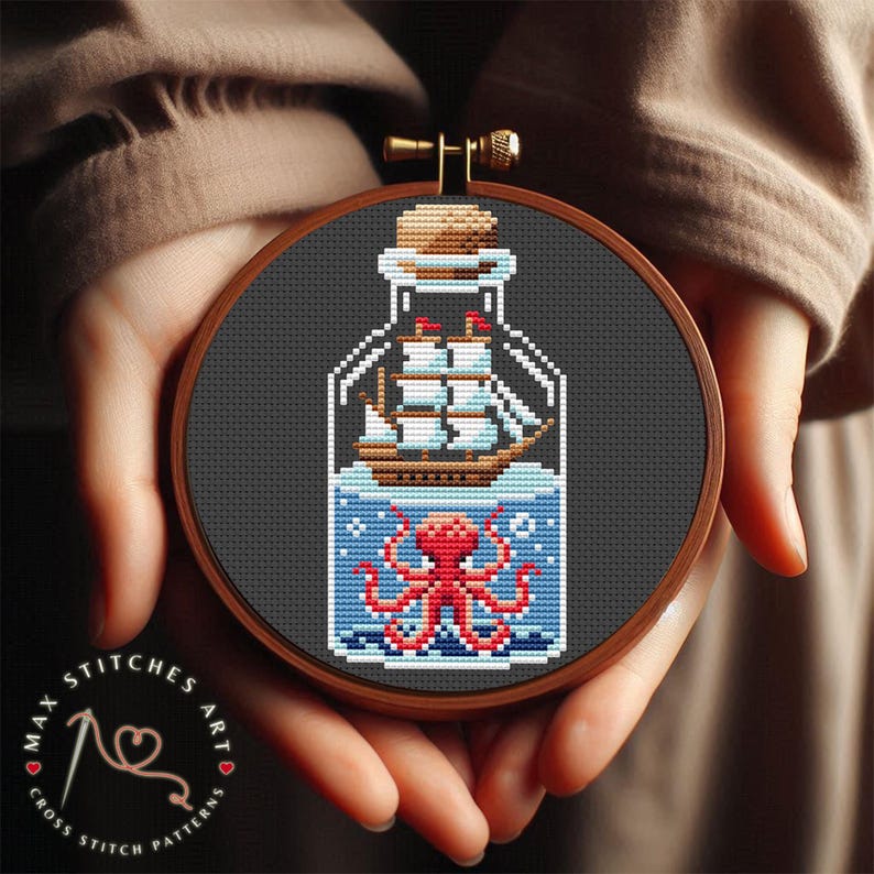 May include: A round wooden embroidery hoop with a black background. Inside the hoop is a cross stitch design of a glass bottle with a ship and an octopus inside. The bottle is blue and white, the ship is brown, and the octopus is red.
