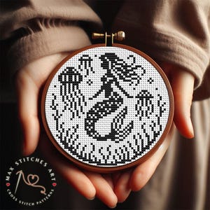 May include: A black and white cross stitch pattern of a mermaid with flowing hair and a tail, surrounded by seaweed. The pattern is displayed in a wooden embroidery hoop.