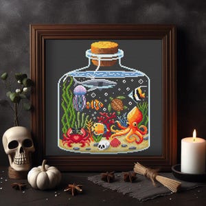 May include: Cross-stitch art of an ocean scene inside a glass bottle with a cork stopper. The scene includes a shark, jellyfish, fish, crab, and octopus. The artwork is framed in a dark wood frame.