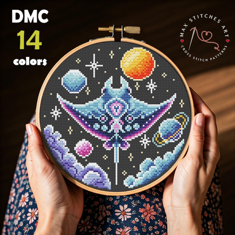 Puede incluir: Un bastidor de bordado de punto de cruz con un dise&ntilde;o celestial. Presenta una manta raya, planetas y estrellas sobre un fondo gris oscuro. El texto "DMC 14 colores" es visible. El bastidor es sostenido por manos.