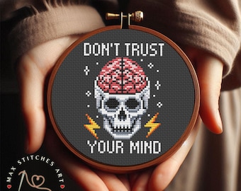 May include: A cross-stitch pattern featuring a skull with a brain inside, surrounded by lightning bolts. The text "Don't Trust Your Mind" is written above the skull.