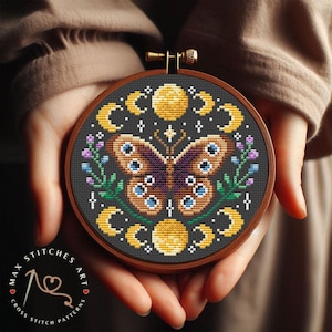 May include: A cross stitch pattern featuring a butterfly with brown and purple wings, surrounded by yellow moons and flowers. The pattern is displayed in a wooden embroidery hoop.